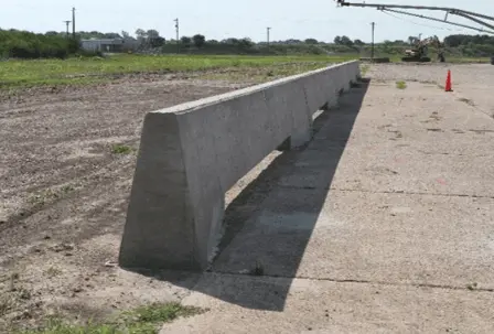 An image of a concrete slotted median barrier separating a parking lot and field.